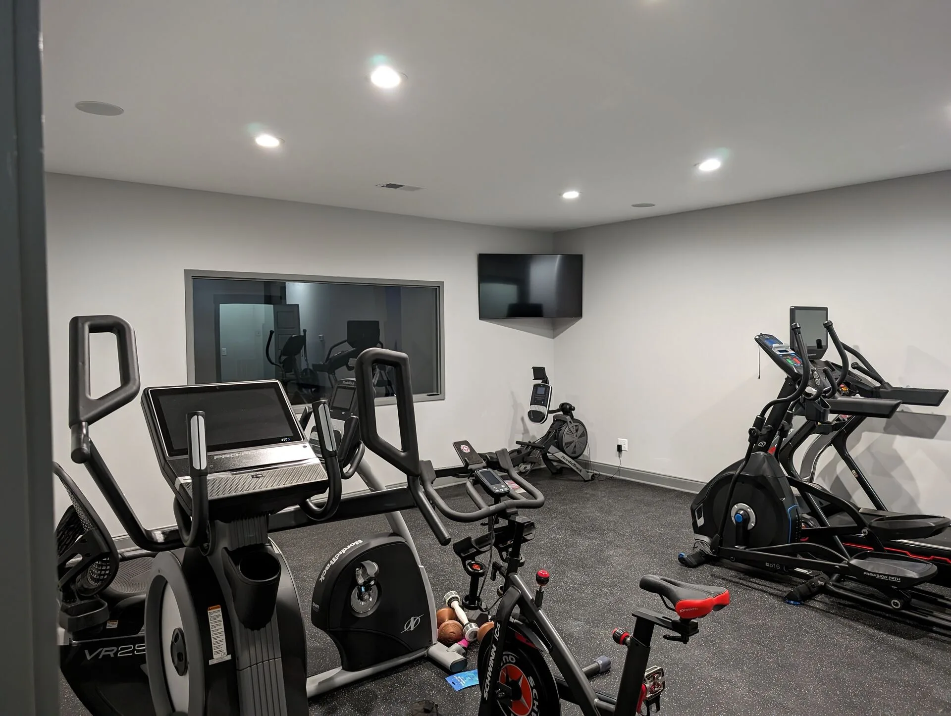 Private home fitness room with Peloton, elliptical, treadmill, and interior window